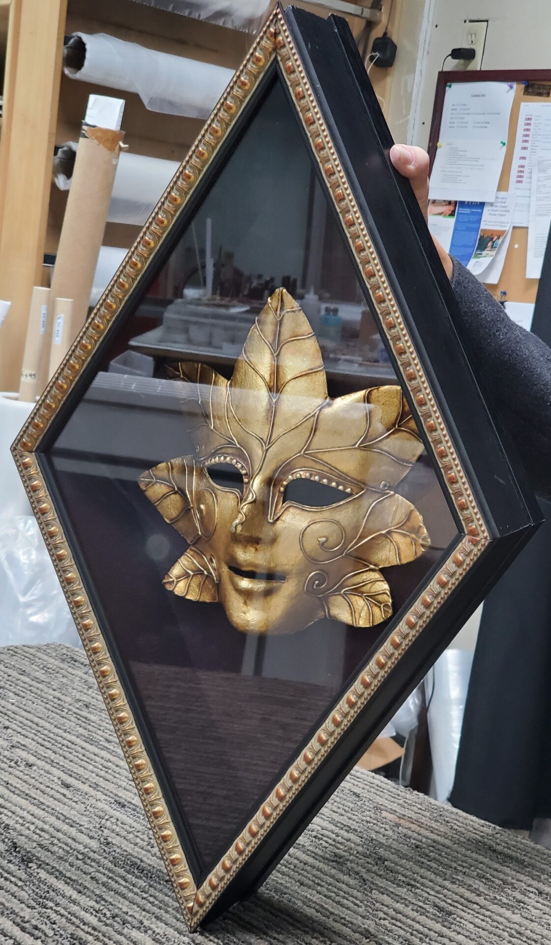 A gold mask is in a black frame.