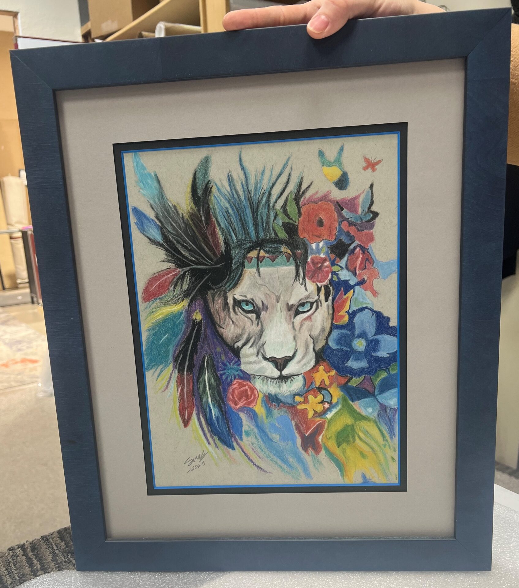 A framed painting of a lion with feathers on it's head.